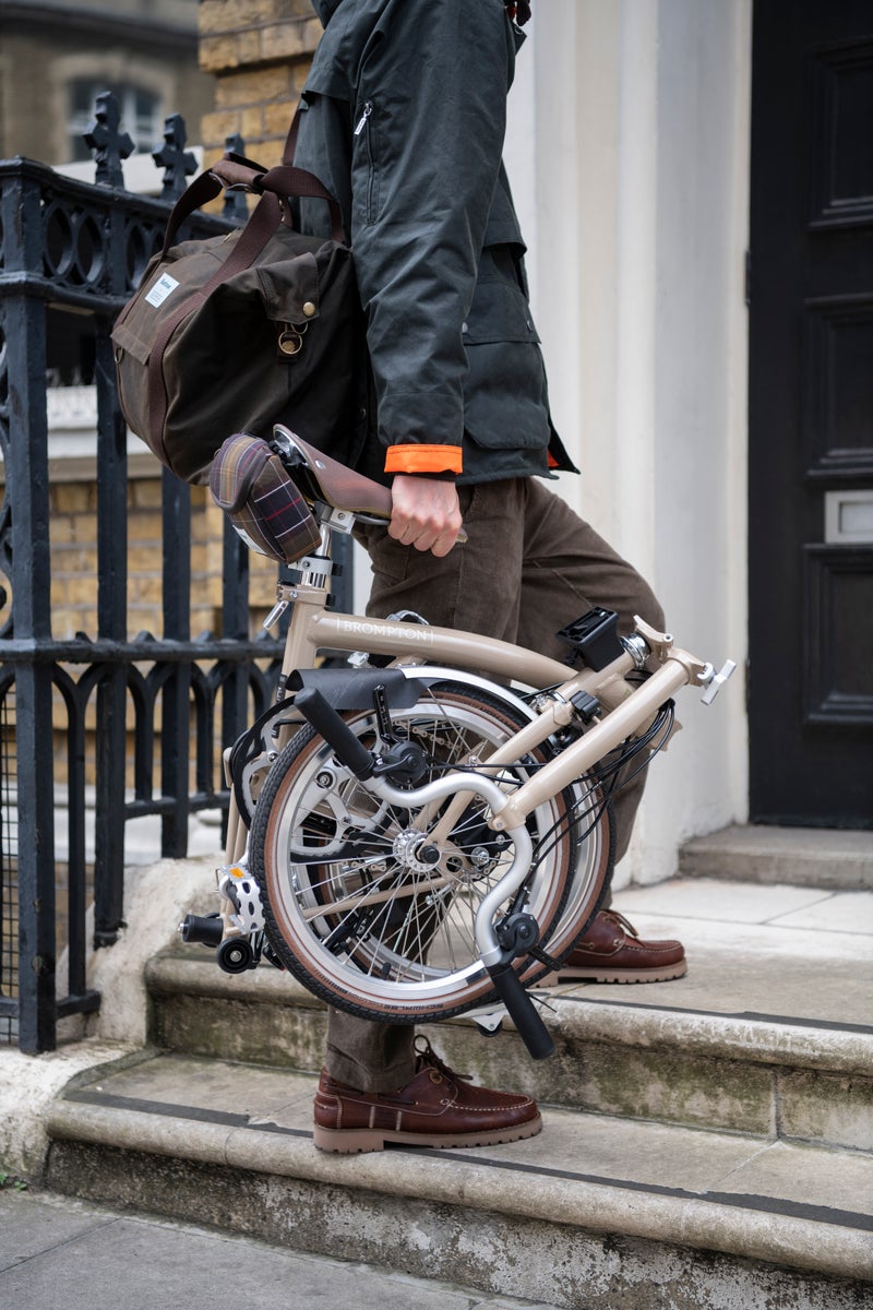 A model posing with a Barbour x Brompton folding bike and a bag from the collection