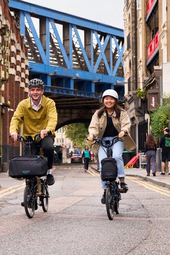 Two happy people riding Brompton Electrics through London