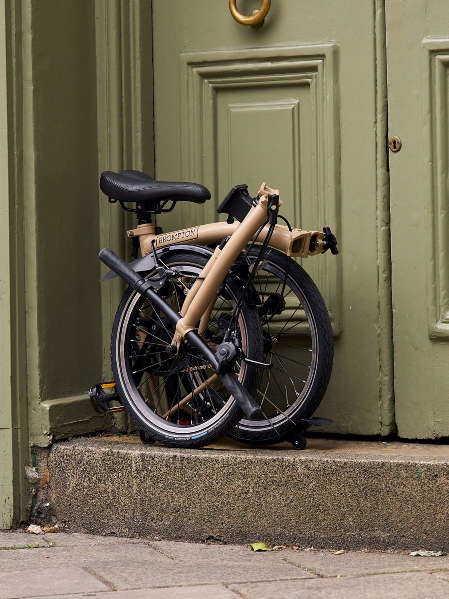 A folded Dune Sands Brompton C Line bike against an earthy neutral door