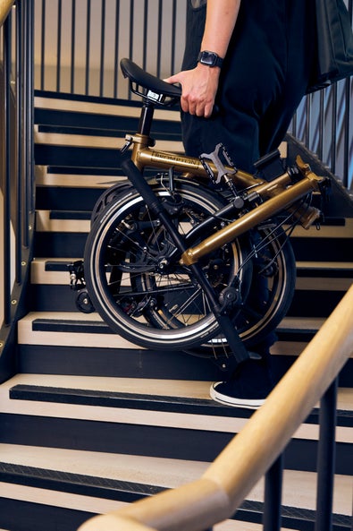 person carrying a folded bronze sky electric p line brompton upstairs