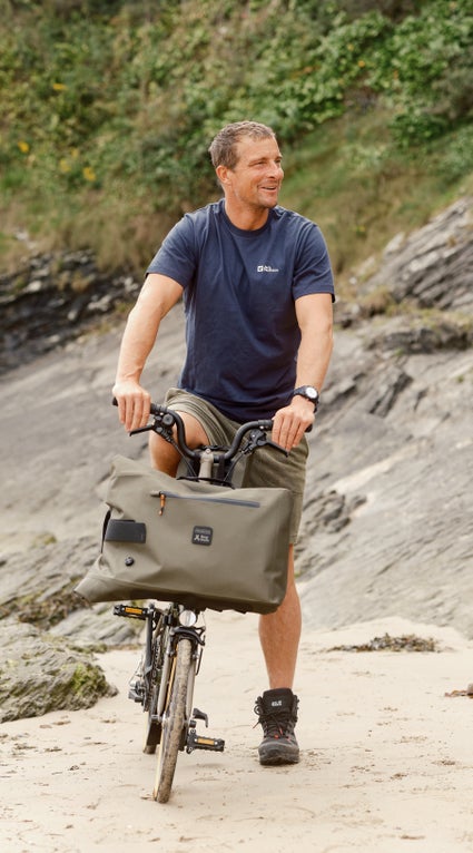 Bear Grylls on his Brompton x Bear Grylls folding bike on the beach