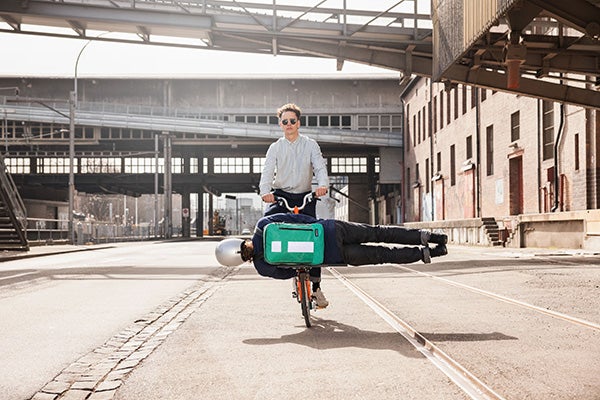 A cyclist riding a Brompton with a gymnast wearing the Freitag x Brompton backpack clipped onto the front of the bike