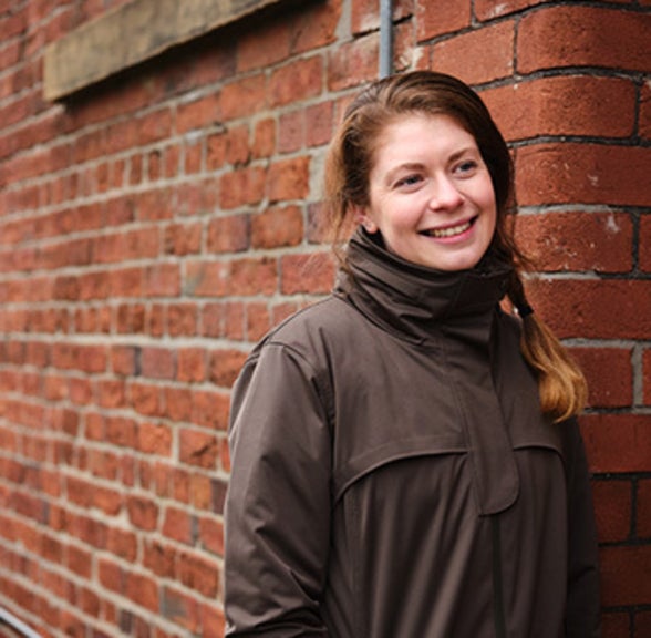 Cyclist Jess Fawcett smiling and posing next to a red brick wall