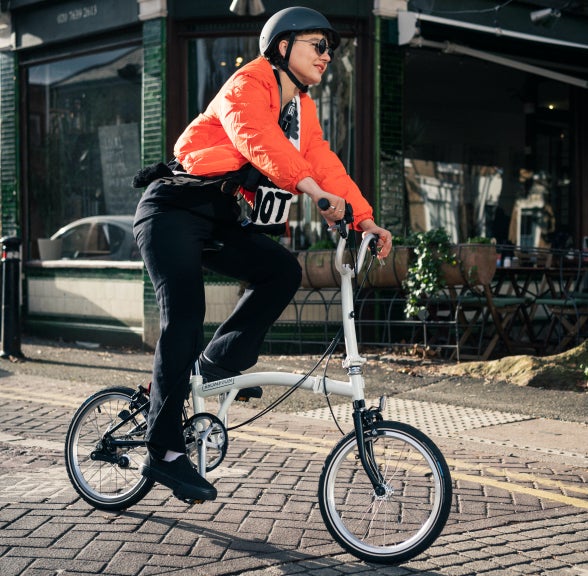 A person in an orange jacket riding a Brompton A Line through the street