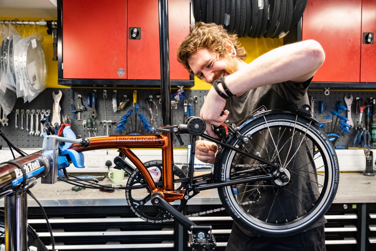 A smiling Brompton mechanic adjusting a tyre in the workshop at Brompton Junction Covent Garden 