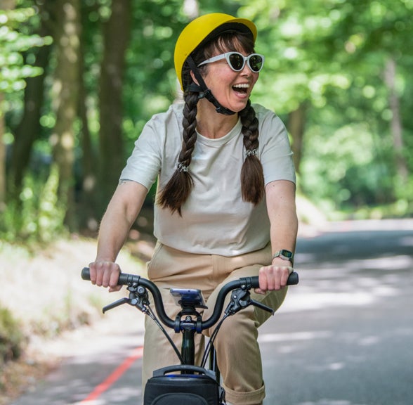 A happy woman laughing and riding a Brompton Electric C Line through the park