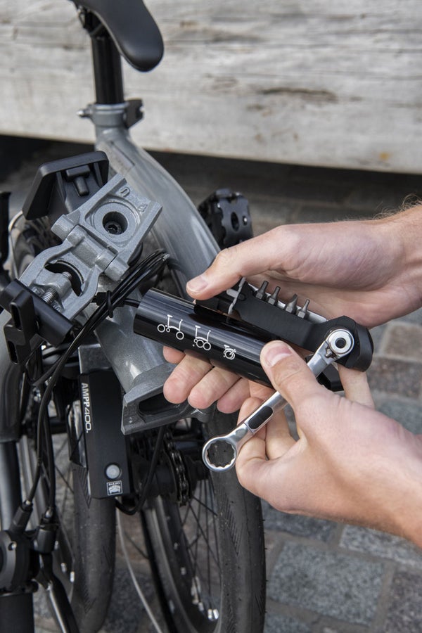 A person holding the Brompton toolkit by the folded Brompton bike